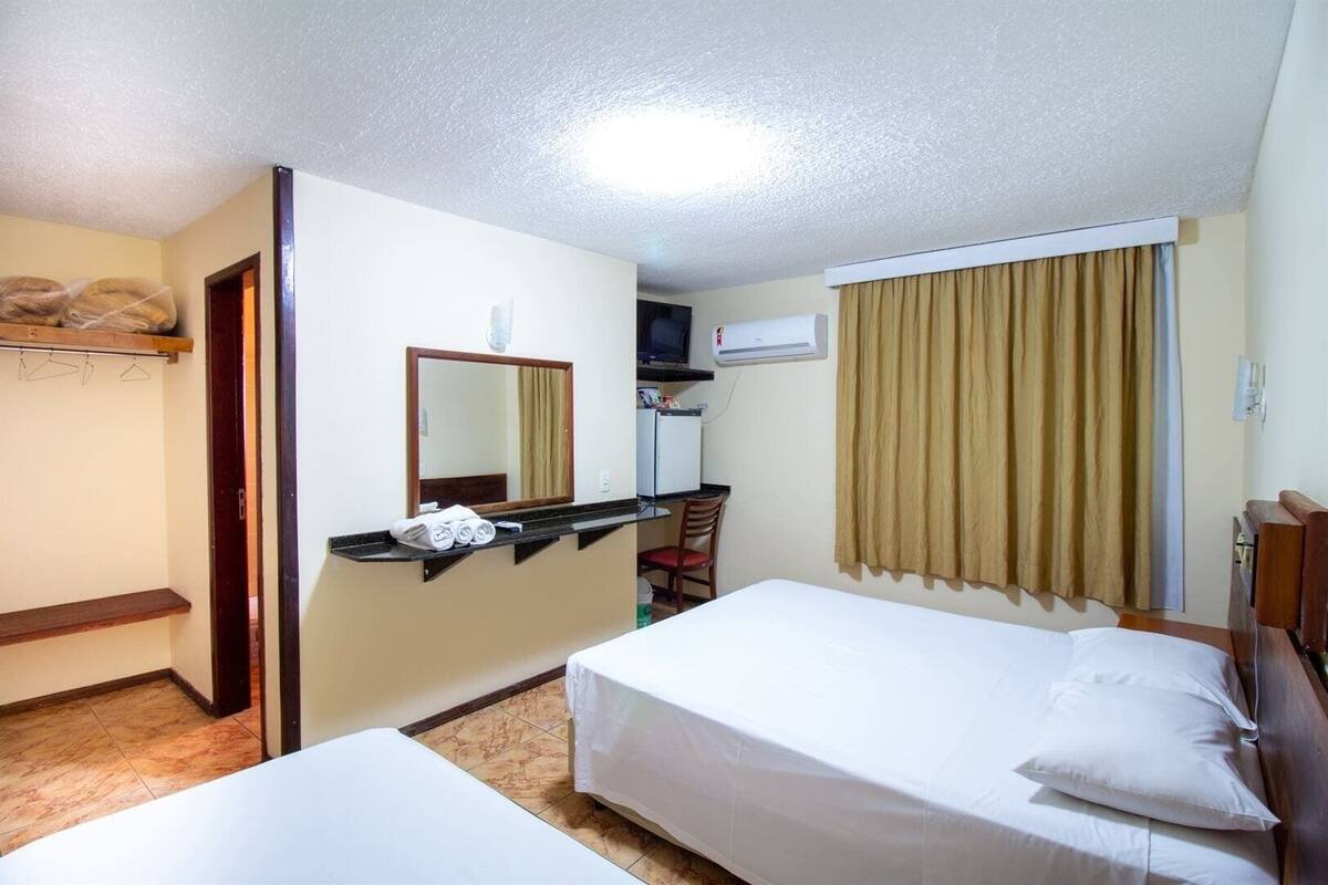 A hotel room with a bed, a desk, a chair, a mirror, and a window with curtains.