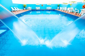 En indendørs swimmingpool med flere baner, hvide liggestole og borde med parasoller.