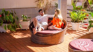 A man and a woman sitting on wicker chairs in a sunlit outdoor area with potted plants and a tiled wall. - Hotel Dan Inn Express Foz do Iguaçu By Nacional Inn (Foz do Iguaçu)