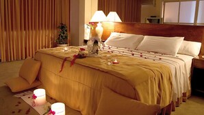 Hotellihuone, jossa on suuri sänky, kaksi yöpöytävalaisinta, yöpöytä ja ikkuna, jossa on verhot.
