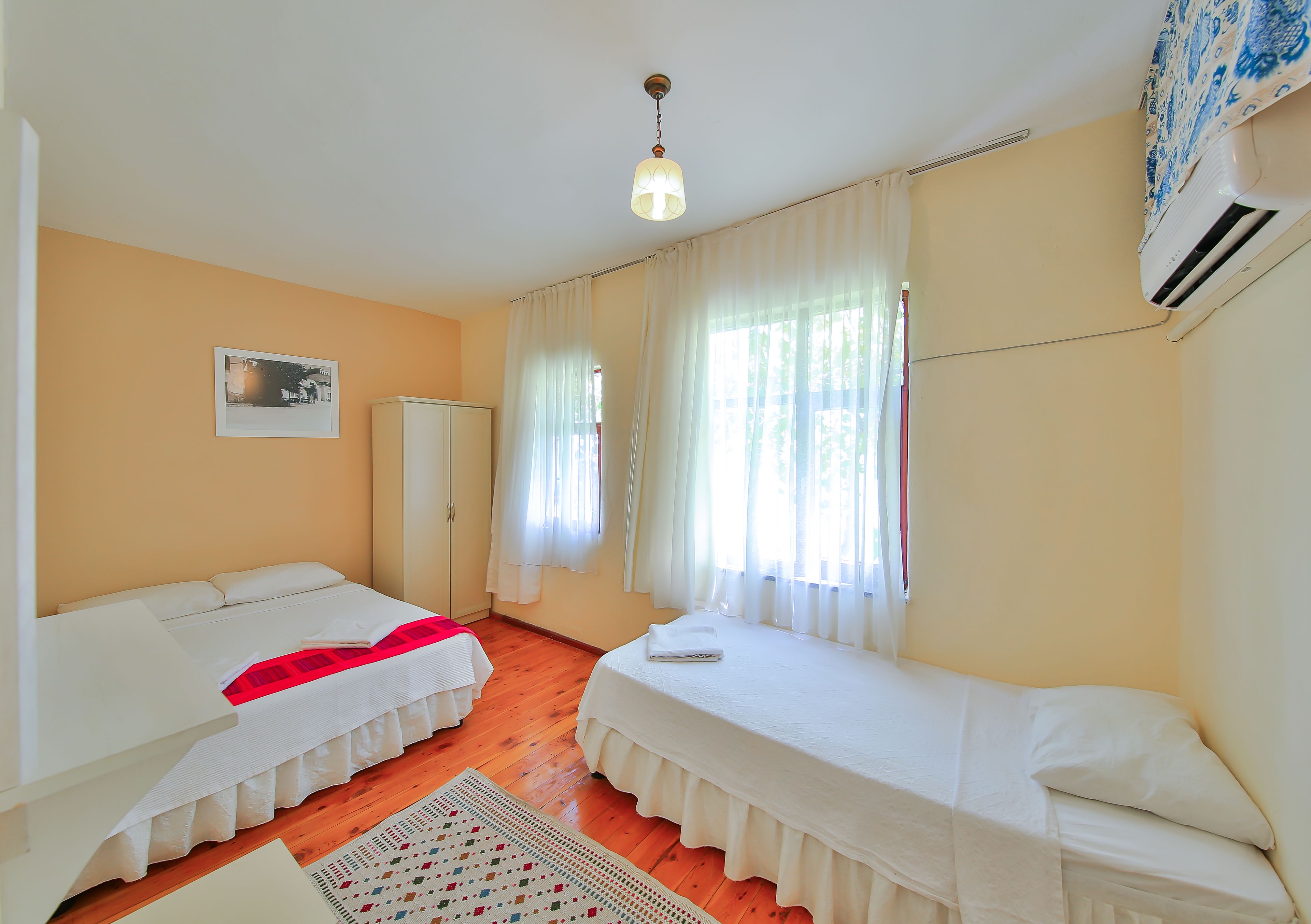 A room with two beds, a wardrobe, a ceiling light, and a window with curtains.