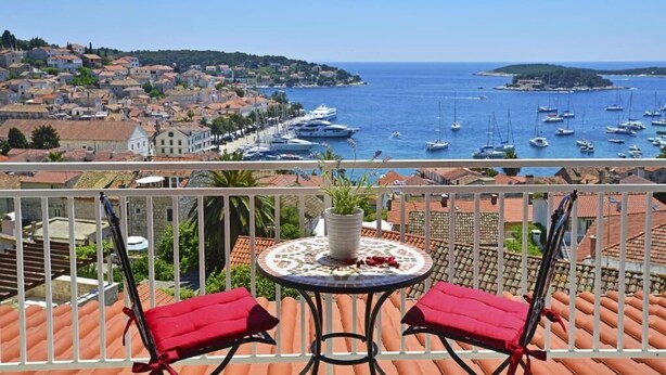 A balcony with a table and chairs, overlooking a marina with boats and a coastal town. - Apartments and Rooms Bonkan Hvar  (Hvar)
