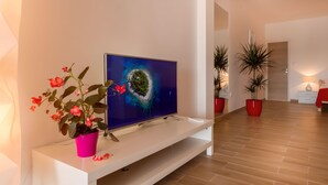 A modern living room with a flat-screen TV on a white console, a pink flower pot, and two potted plants. - Apartments and Rooms Bonkan Hvar  (Hvar)