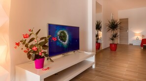 A modern living room with a flat-screen TV on a white console, a pink flower pot, and two potted plants. - Apartments and Rooms Bonkan Hvar  (Hvar)