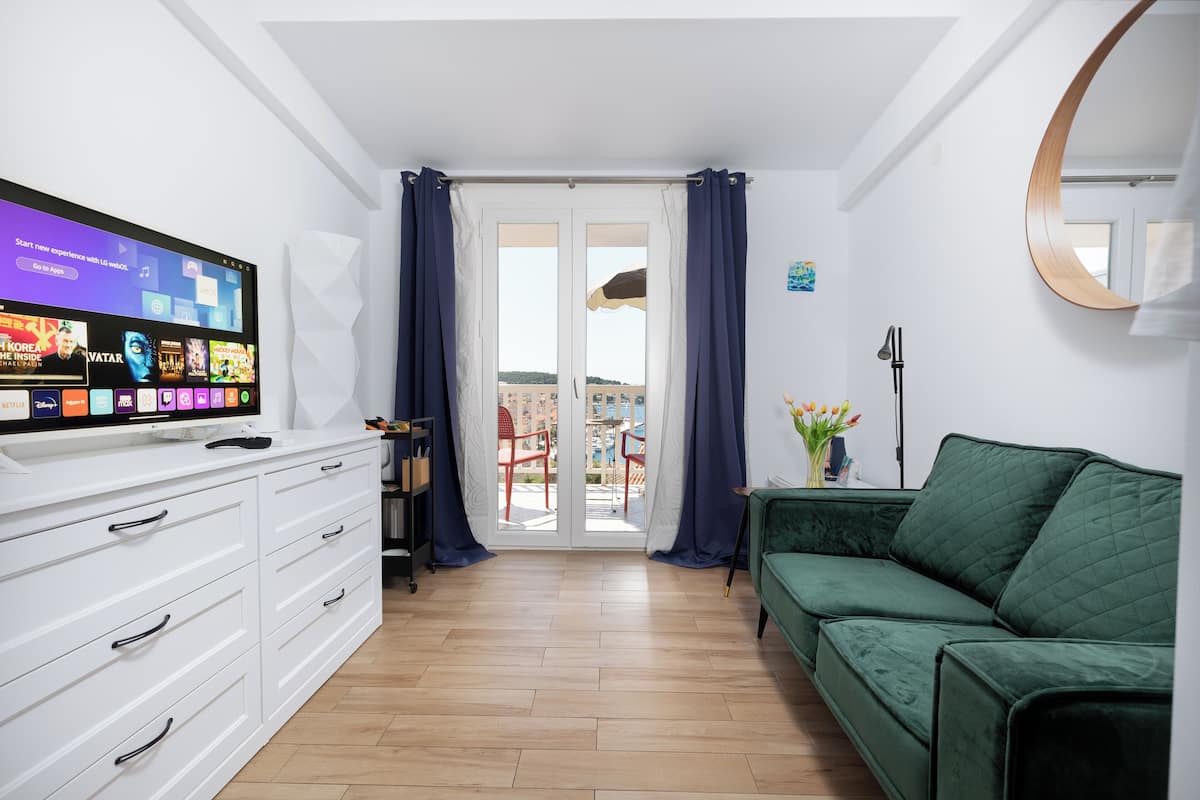Una sala de estar moderna con televisor de pantalla plana, muebles blancos, un sofá verde y un balcón con sillas rojas.