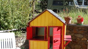 A small, yellow wooden shed with red trim, situated next to a stone wall and a white chair. - Hotel delle Alpi (Sondalo)