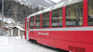 A red and white train with 'Ferrovia retica' written on the side, parked on a snowy track with mountains in the background. - Hotel delle Alpi (Sondalo)