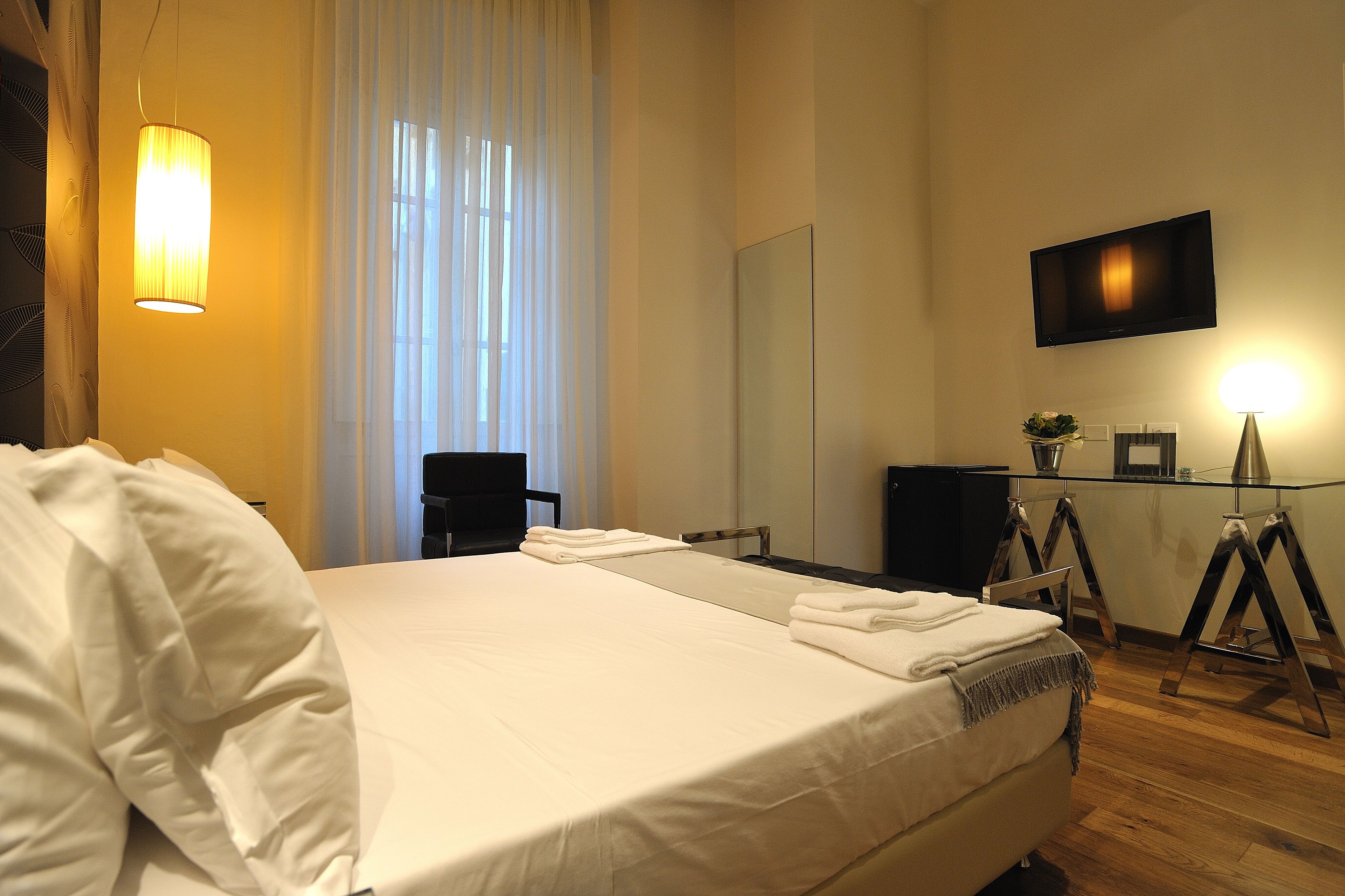 A hotel room with a large bed, a desk, a chair, a television, and a mirror.