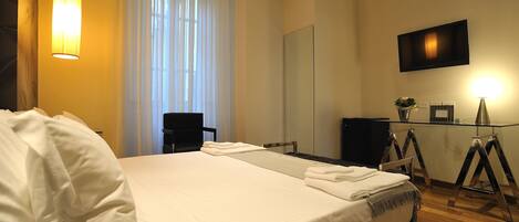 A hotel room with a large bed, a desk, a chair, a television, and a mirror.