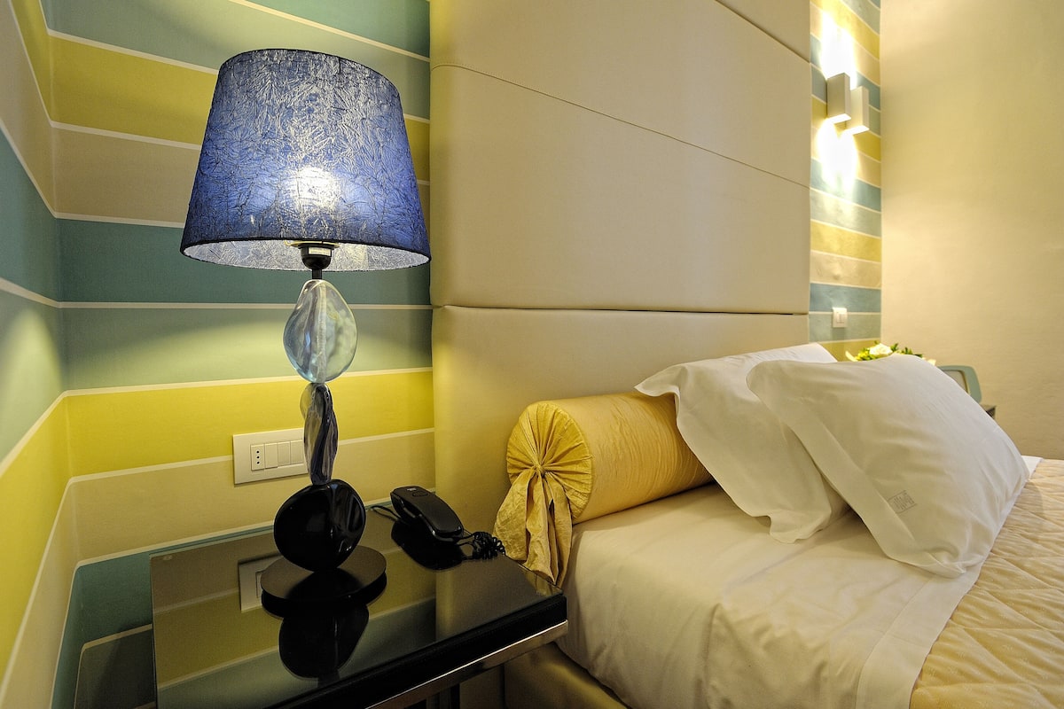 Een hotelkamer met een bed, een nachtkastje met een lamp en een muur met een strepenpatroon.