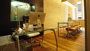 A modern office with a glass desk, an Apple iMac, a lamp, and a view of the city through a window.