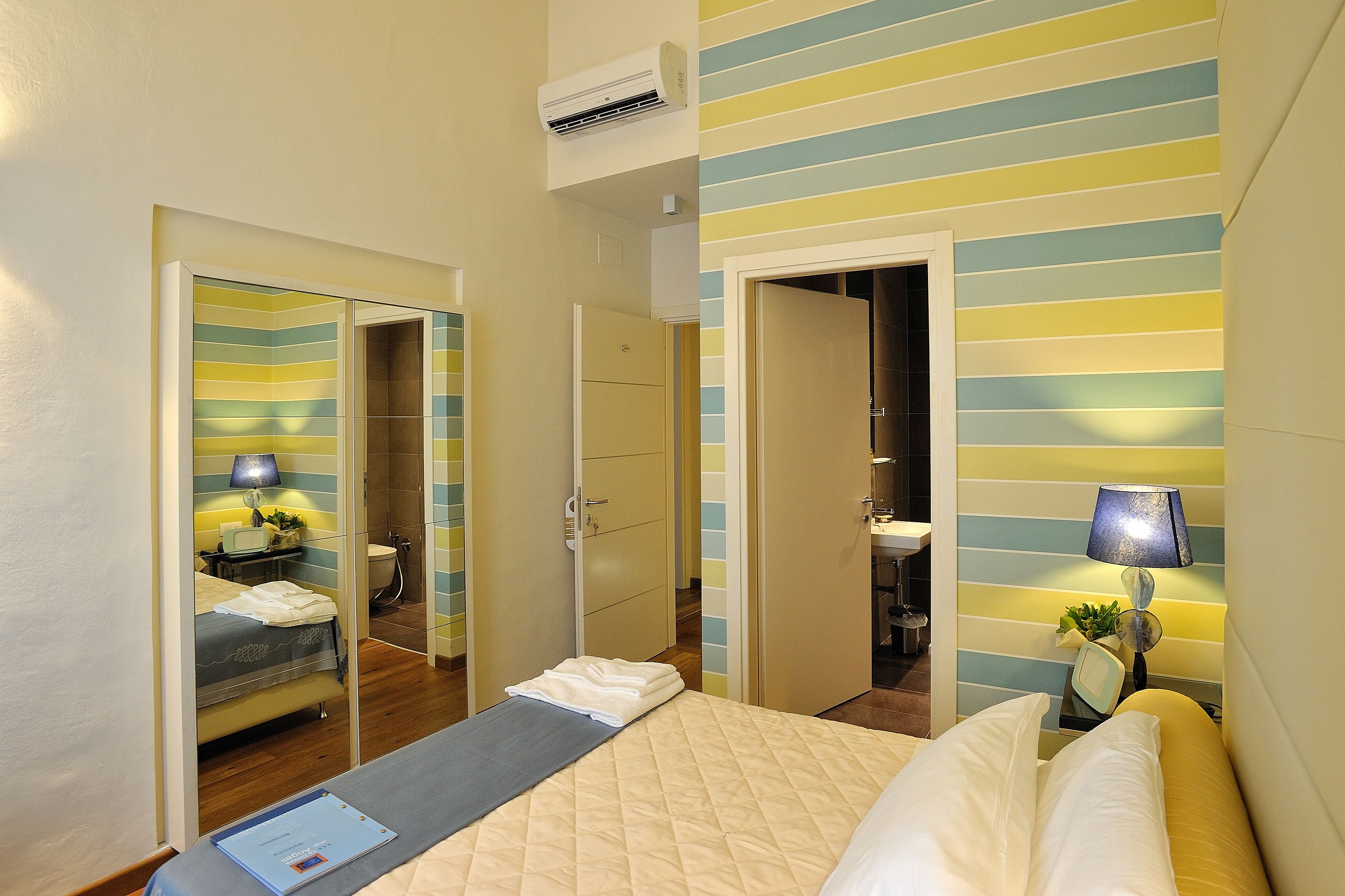 Camera d'albergo con un letto, una scrivania, uno specchio, un armadio e un bagno visibile attraverso una porta aperta.