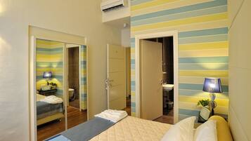Camera d'albergo con un letto, una scrivania, uno specchio, un armadio e un bagno visibile attraverso una porta aperta.