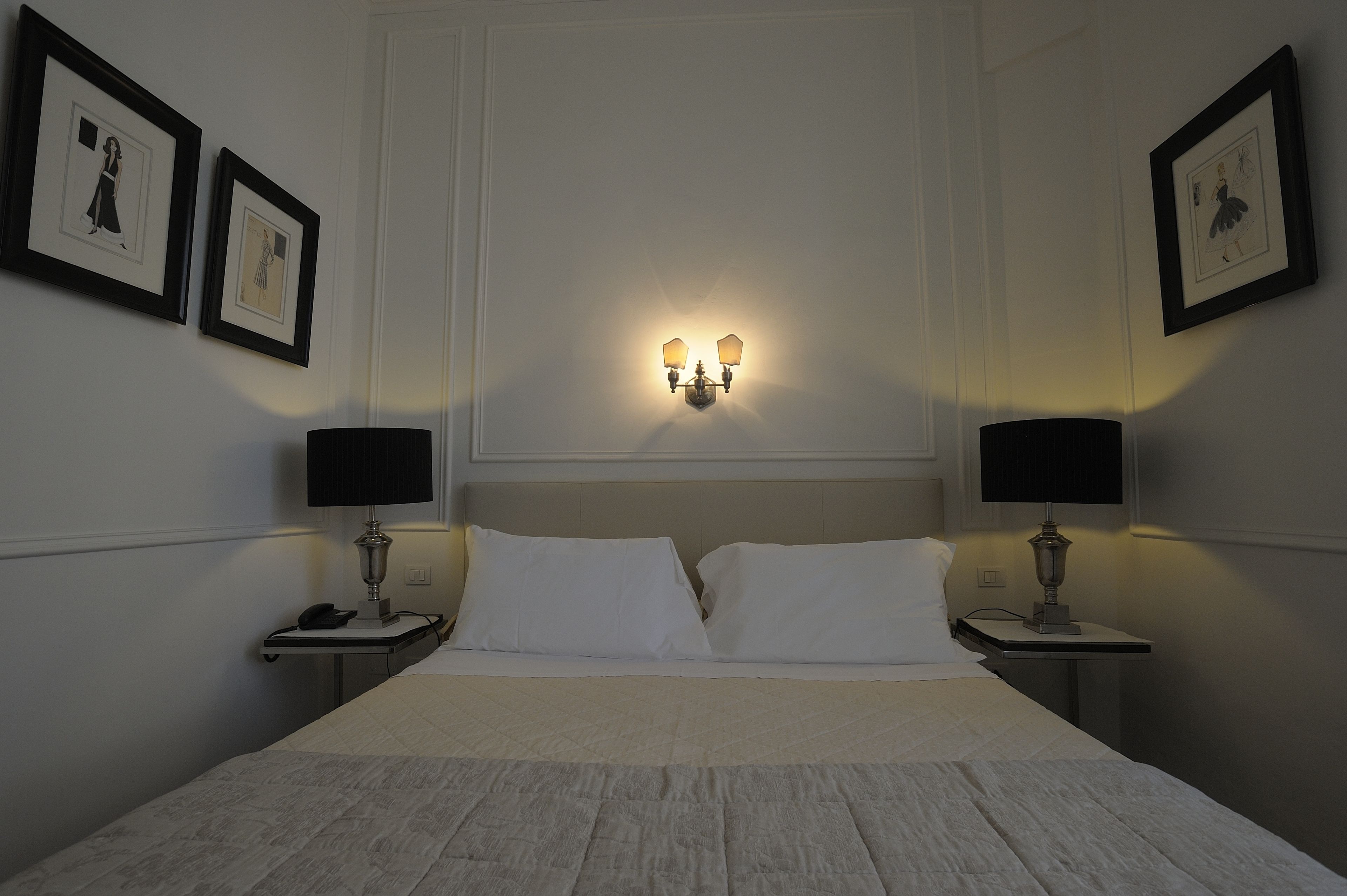 Ein Hotelzimmer mit einem großen Bett, zwei Nachttischen mit Lampen und gerahmten Bildern an den Wänden.
