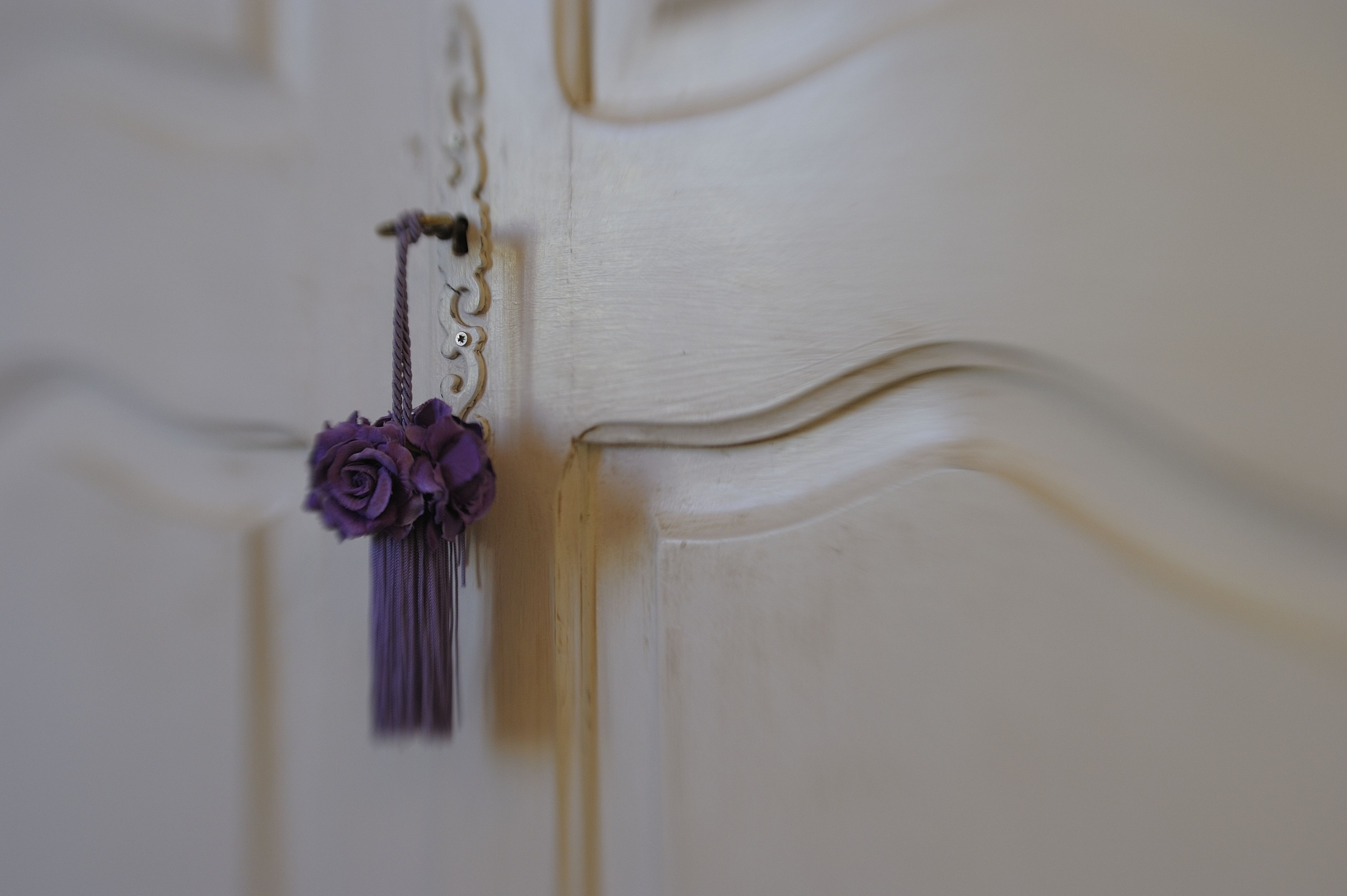 A close-up of a white door with a decorative keychain featuring a purple flower and tassel.