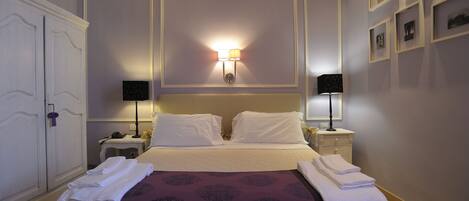 A neatly made bed with white linens, two bedside tables with lamps, a wardrobe, and framed pictures on the wall.