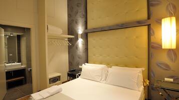 A hotel room with a bed, a bedside table, a mirror, a bathroom with a sink, and a wall with a leaf pattern.