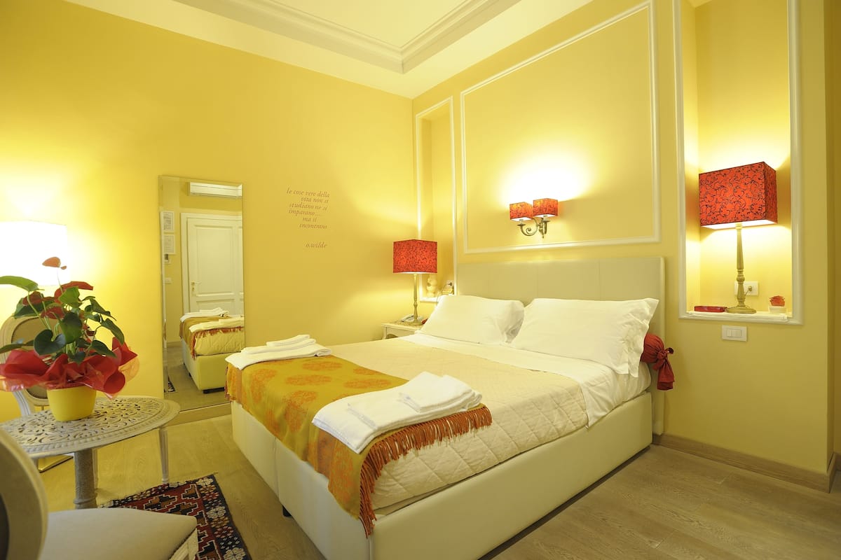 Een hotelkamer met een bed, nachtlampjes, een klein tafeltje met een plant en een spiegel.