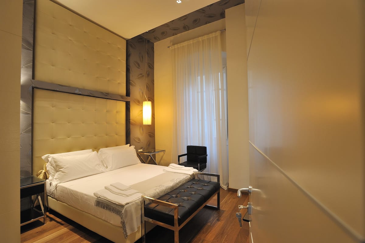 Een moderne hotelkamer met een groot bed, een nachtkastje, een stoel en een bankje.