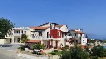 Un edificio de varios pisos con fachada roja y blanca, una piscina visible y una vista despejada del mar al fondo.