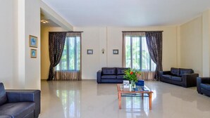 A spacious living room with a black leather sofa set, a wooden coffee table, and a large window with curtains. - Antilia Apts (Platanias)