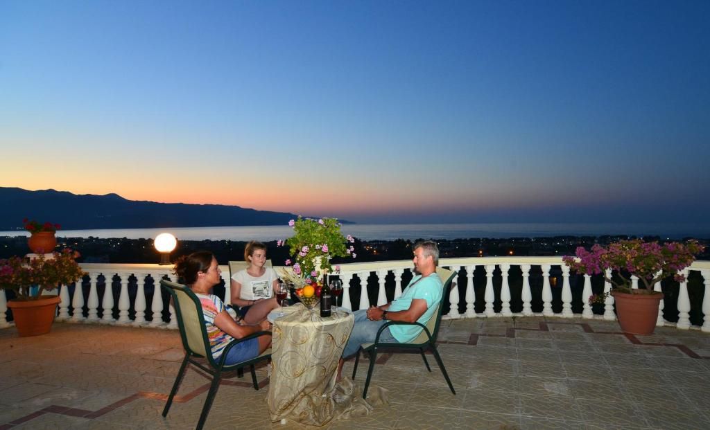 A terrace with a table set for two, overlooking a body of water and mountains at dusk.