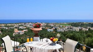A balcony with a table set for breakfast, overlooking a coastal town and the sea. - Antilia Apts (Platanias)