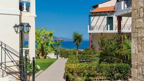 A narrow pathway leading to a building with a balcony overlooking a coastal view. - Antilia Apts (Platanias)