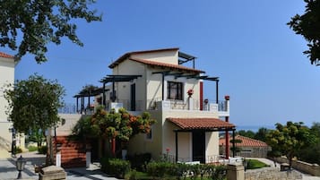 A two-story building with a balcony, a covered porch, and a view of the sea.