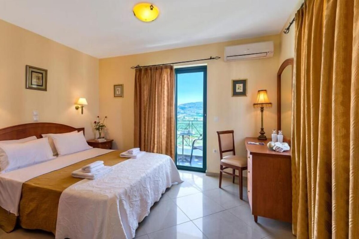 A hotel room with a bed, a desk, a chair, a balcony with a view, and an air conditioning unit.