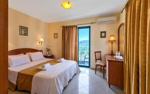 A hotel room with a bed, a desk, a chair, a balcony with a view, and an air conditioning unit. - Antilia Apts (Platanias)