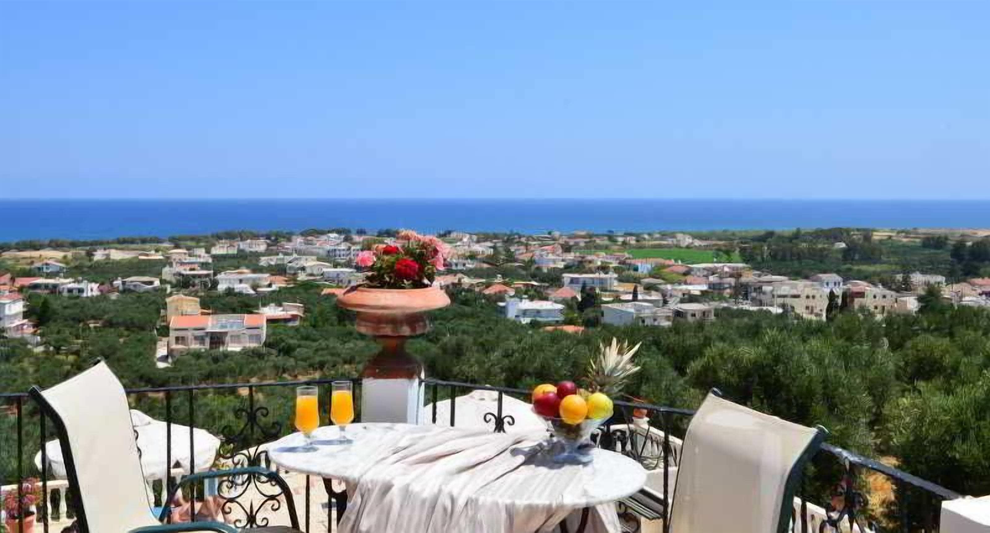 A balcony with a table set for dining, overlooking a coastal town and the sea.