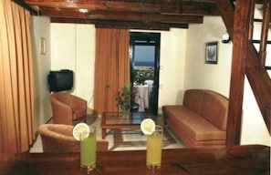 A living room with a sofa, armchair, and a coffee table. There is a television on a stand, and a balcony with a view. - Antilia Apts (Platanias)
