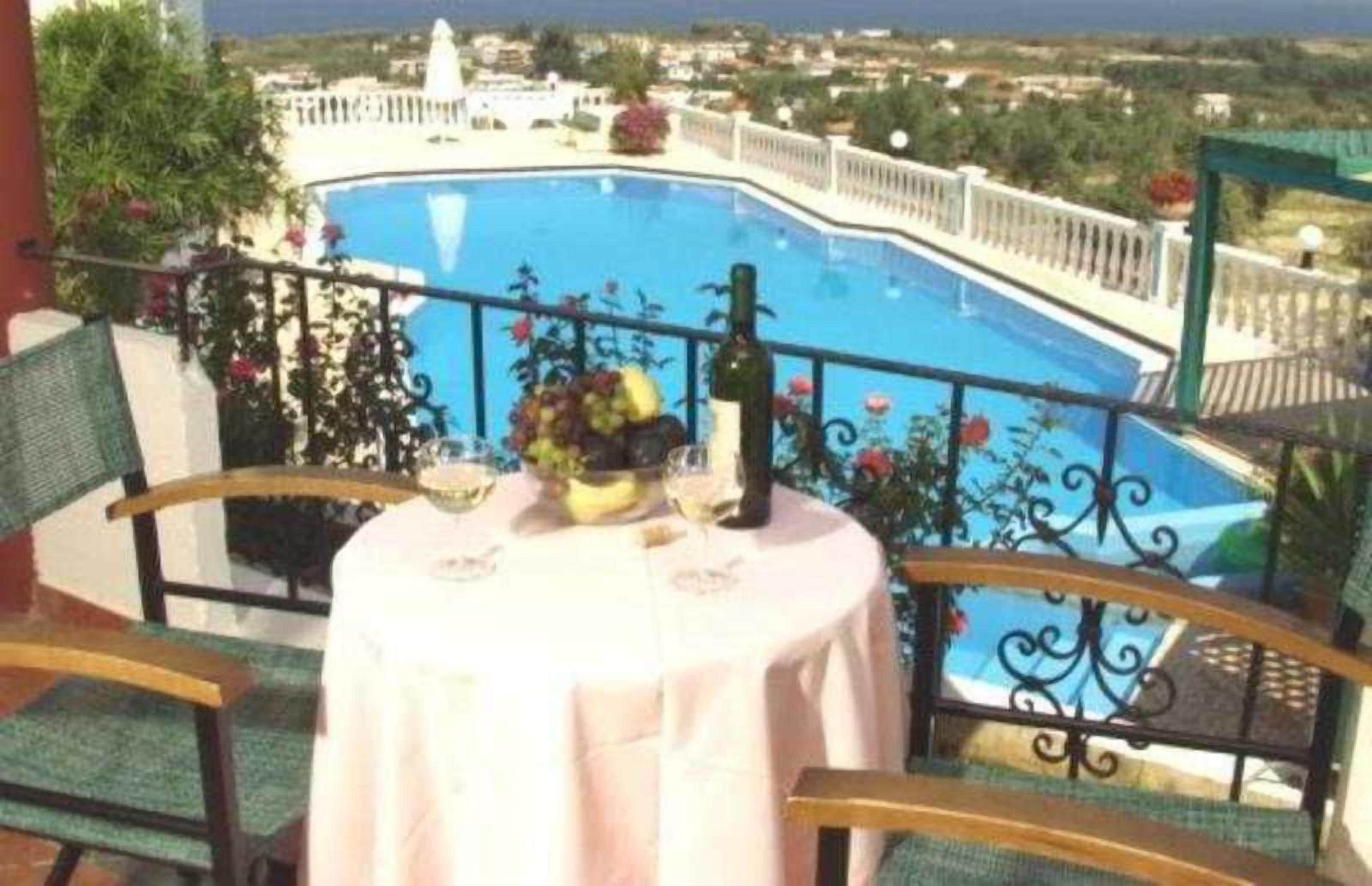 Un balcón con mesa lista para dos personas, con vista a una piscina.