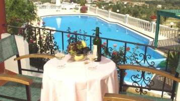 Un balcón con mesa lista para dos personas, con vista a una piscina.