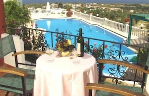 A balcony with a table set for two, overlooking a swimming pool. - Antilia Apts (Platanias)