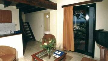Una sala de estar con televisión, una mesa con una planta y vistas a través de un ventanal.