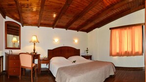 A bedroom with a wooden ceiling, a bed with a beige bedspread, a desk with a lamp, a chair, and a nightstand with a vase. - Antilia Apts (Platanias)