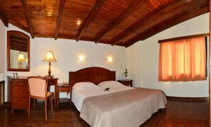 A bedroom with a wooden ceiling, a bed with a beige bedspread, a desk with a lamp, a chair, and a nightstand with a vase. - Antilia Apts (Platanias)