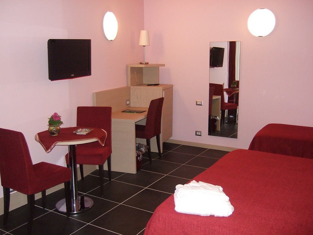 Habitación de hotel con cama, escritorio, silla, una mesita con un florero y espejo.