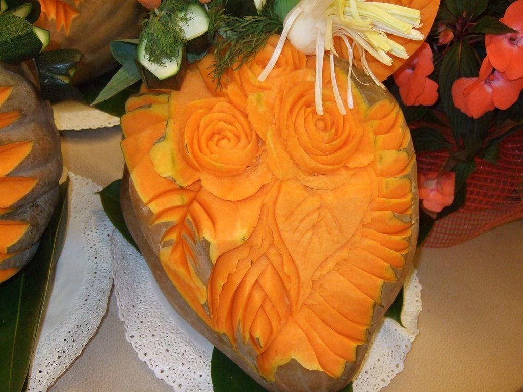 Une sculpture représentant un kaki, ornée de motifs complexes, et entourée d’éléments décoratifs tels que des fleurs et du feuillage.