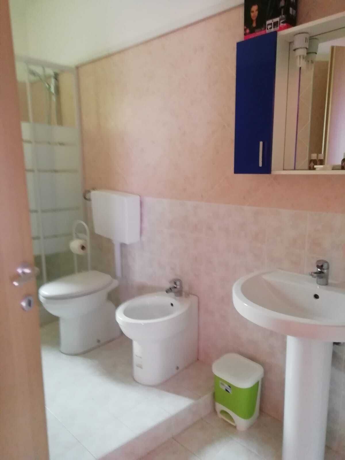 Un bagno con un water, un bidet, un lavandino e un piccolo cestino.