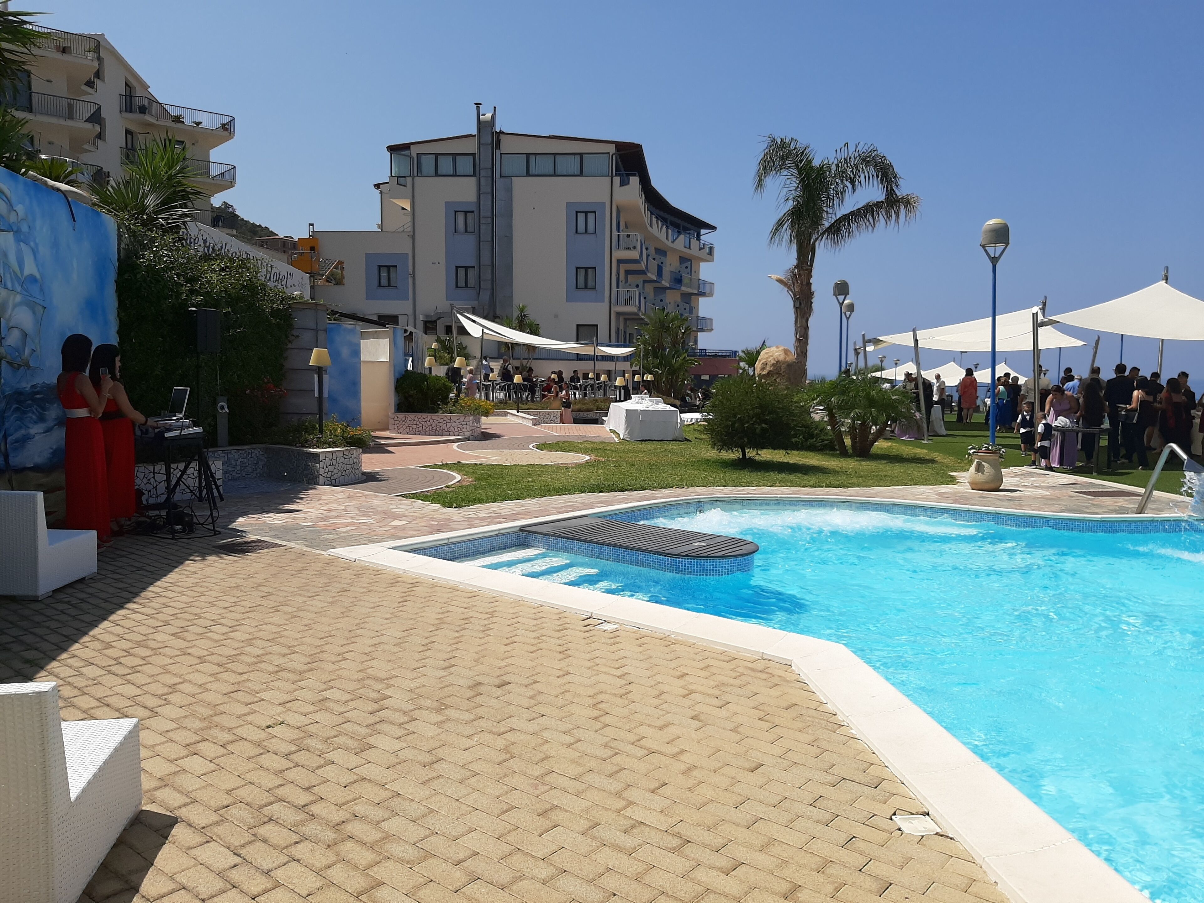 A swimming pool area with a tiled deck, a lounge chair, and a building with balconies in the background.