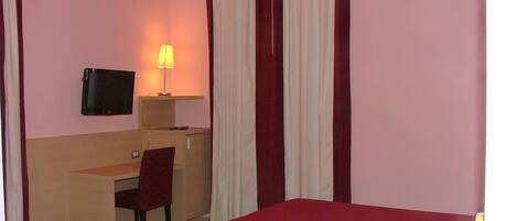 Een hotelkamer met een bed, bureau, stoel, televisie en lamp.