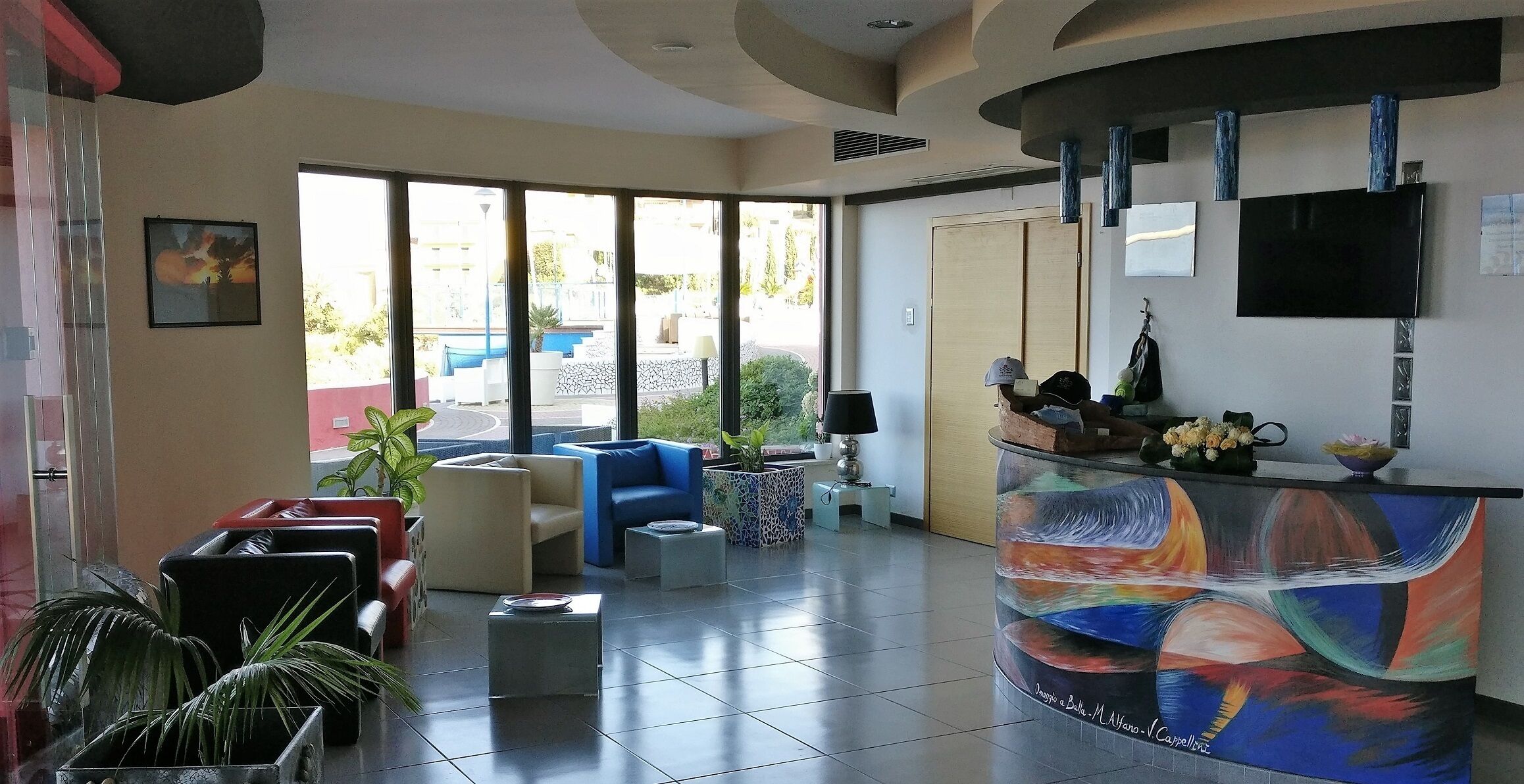 Un hall d’hôtel moderne doté d’un comptoir d’accueil, d’un espace salon et de grandes fenêtres offrant une vue sur l’extérieur.
