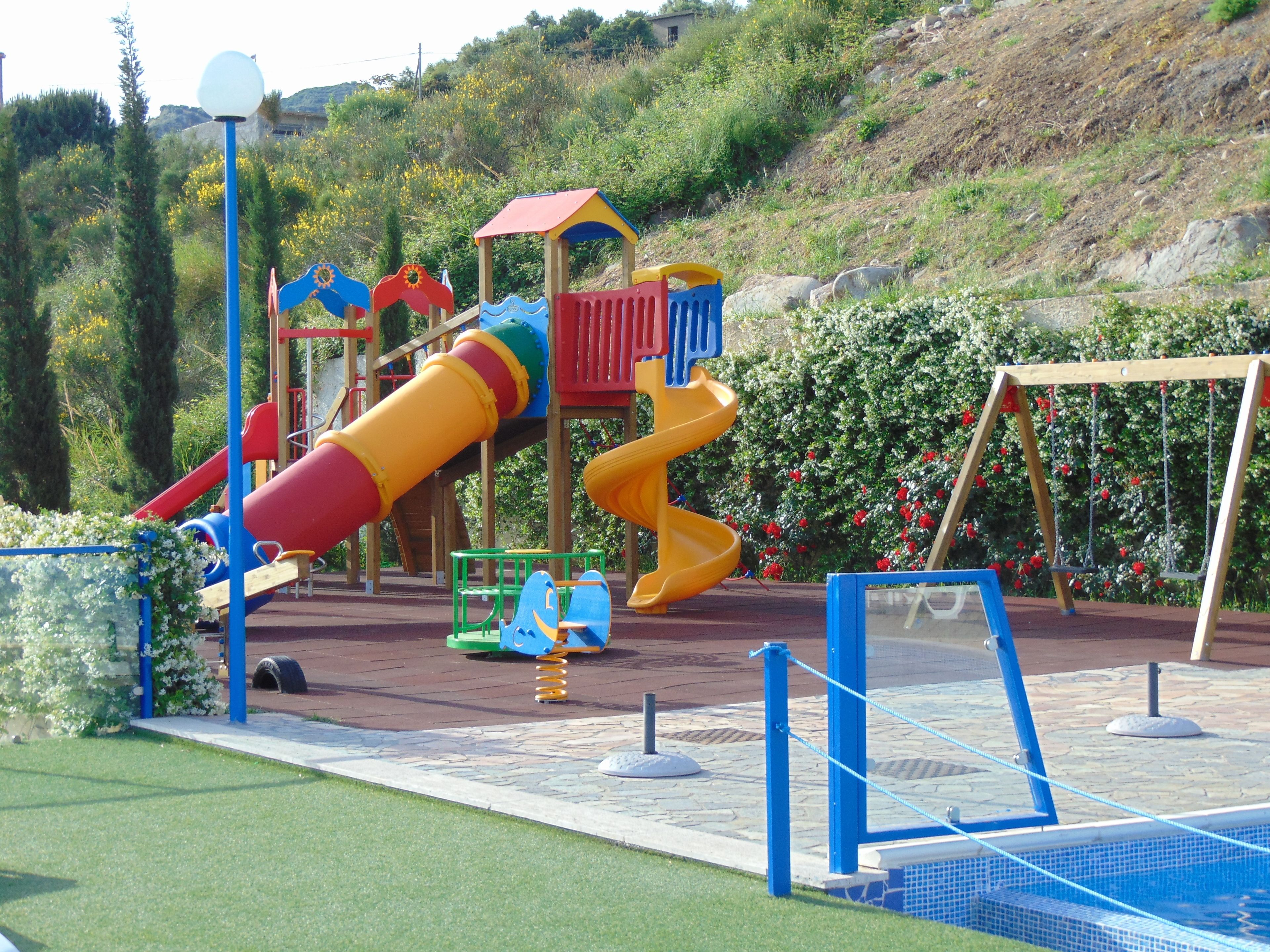 Un parque infantil con toboganes y columpios, rodeado de vegetación y un paisaje montañoso.
