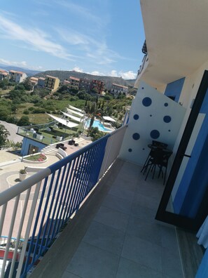 A balcony with a pool view, blue railing, and a dining area with chairs. - Tus' Hotel (Tusa)