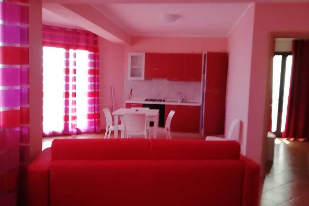 Una sala moderna con un sofá rojo, una mesa de comedor con sillas y una zona de cocina con armarios rojos.