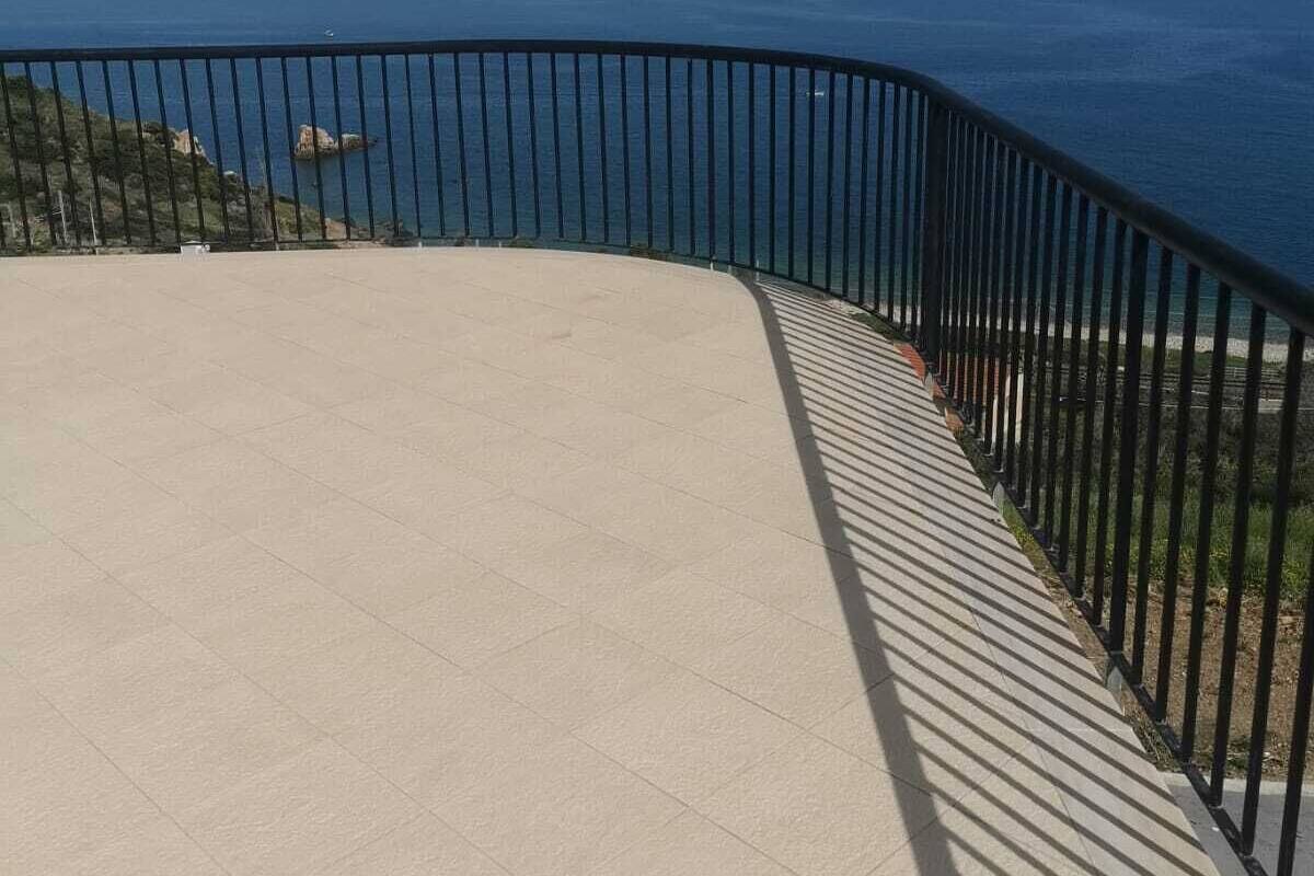 Una terraza con vista al océano, barandilla curva de metal negro y suelo de baldosas.