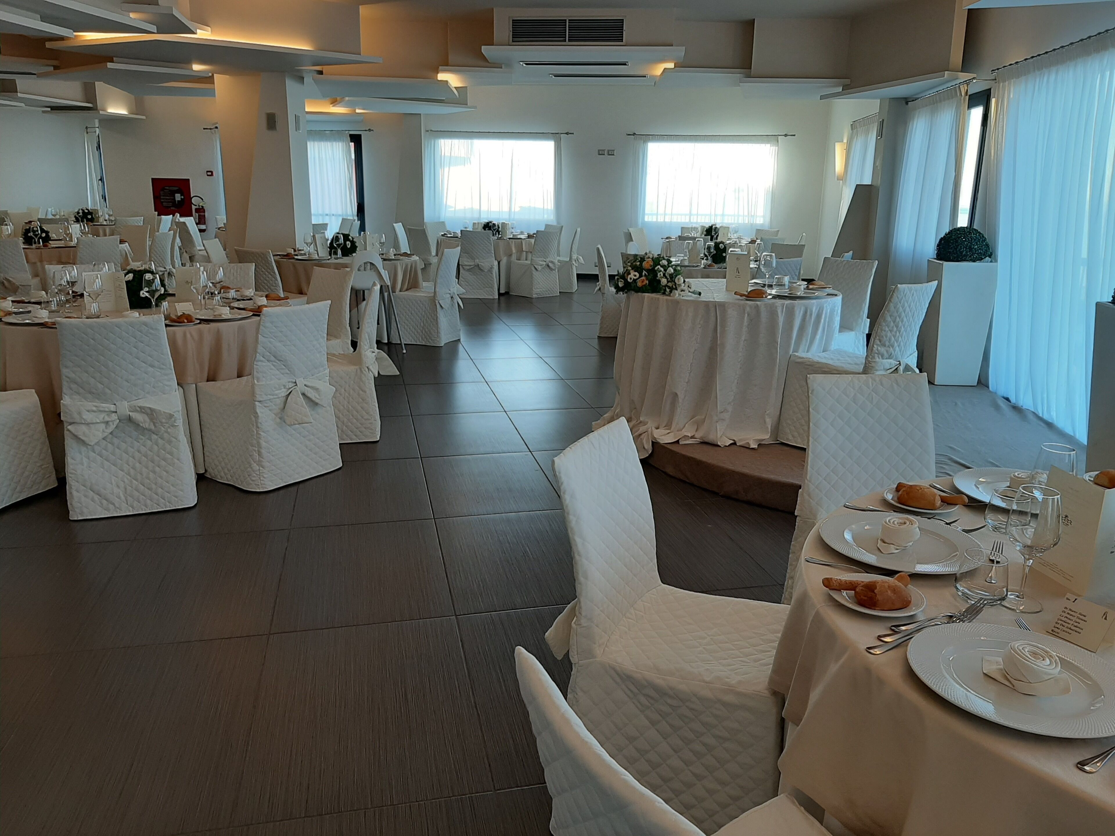 A banquet hall with round tables, white chairs, and a tiled floor.